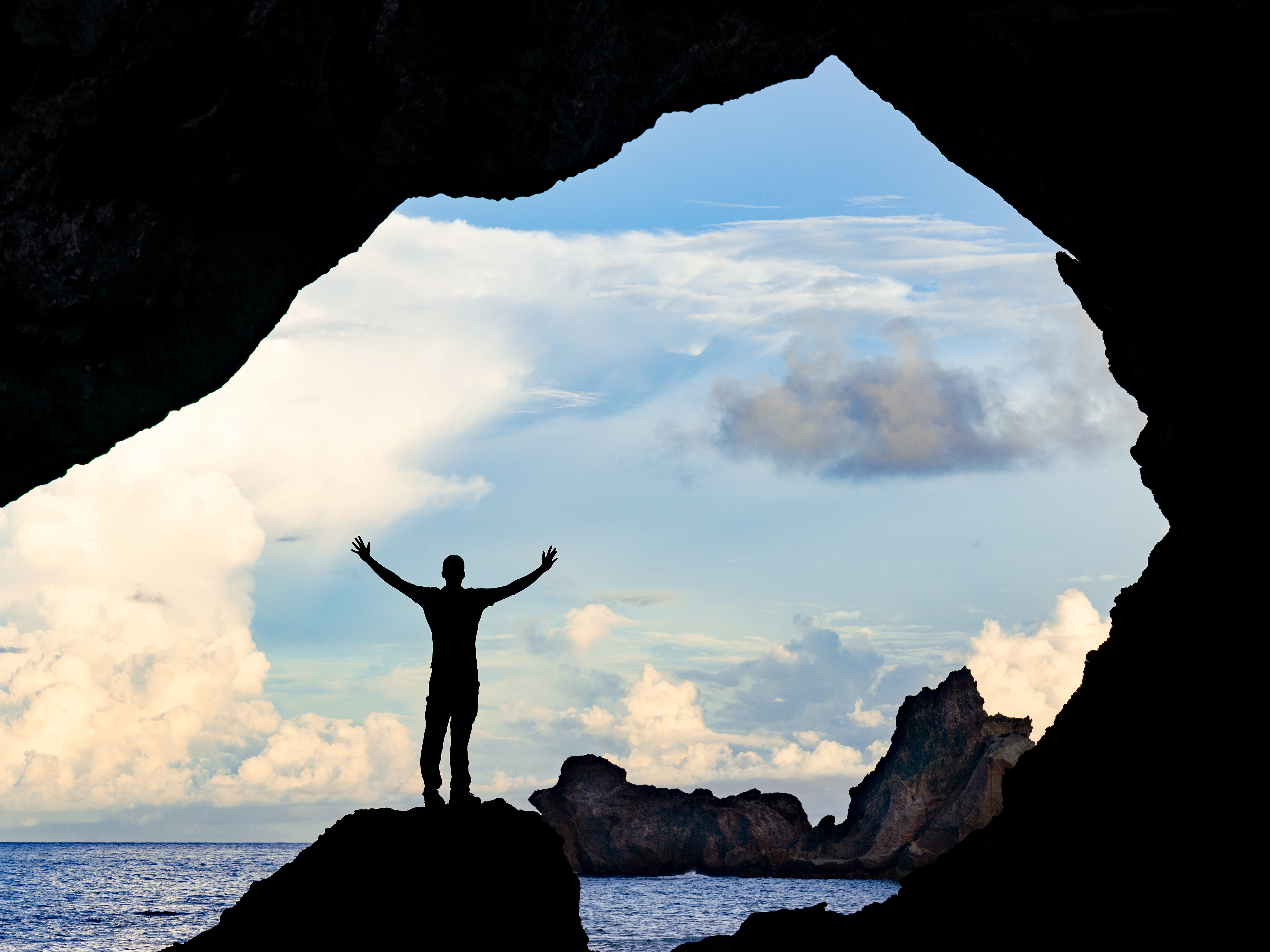 Person raising arms in ocean cave